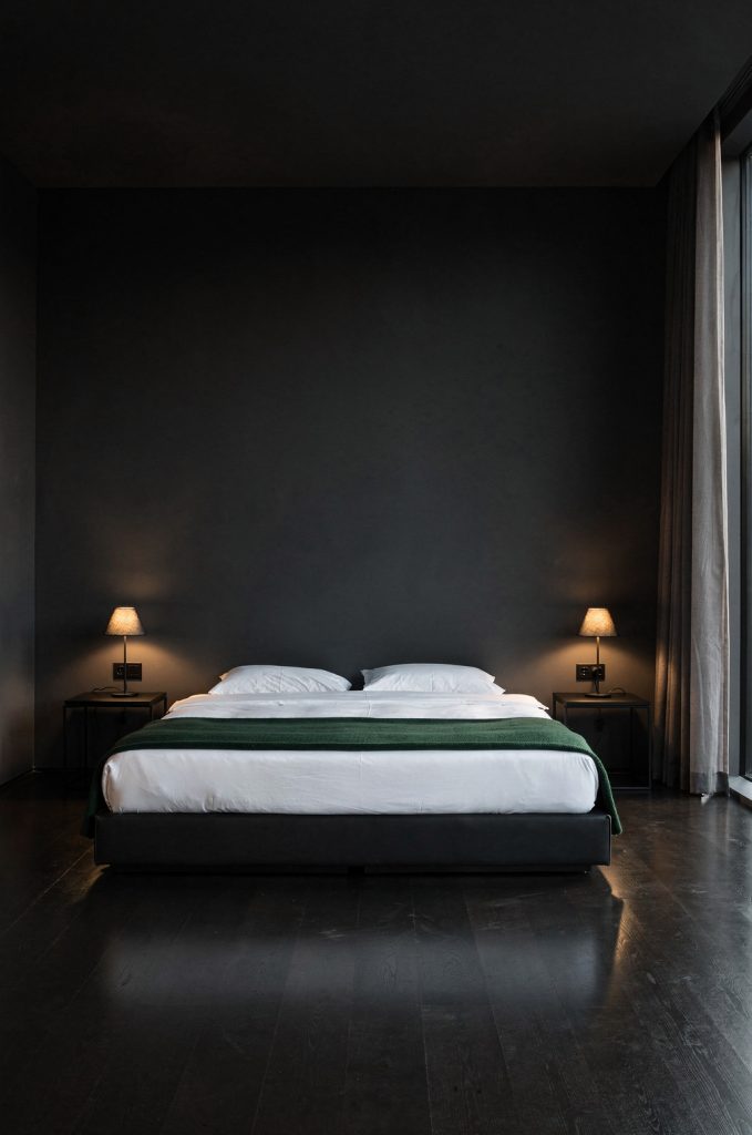Minimalist bedroom with grey walls, green throw blanket, and warm bedside lighting creating a modern contrast.