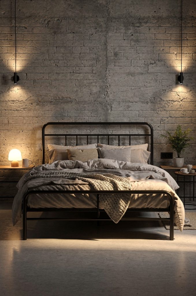 Industrial bedroom with black metal bed frame, layered neutral bedding, warm lighting, and textured wall.