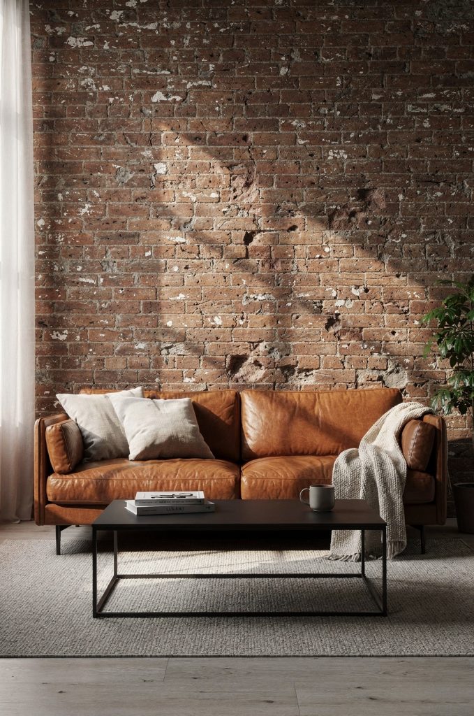 Industrial living room with exposed brick wall, brown leather sofa, black metal coffee table, and soft neutral textiles.