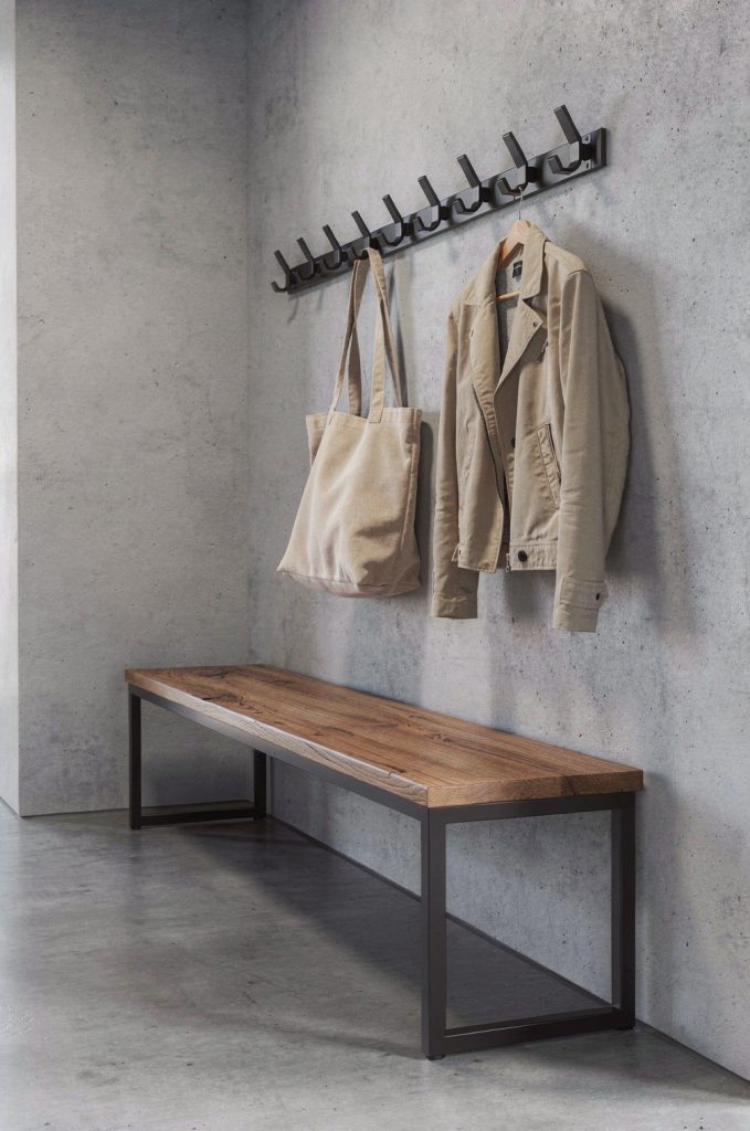 Industrial entryway with wooden bench, black metal frame, wall hooks, and concrete wall background.